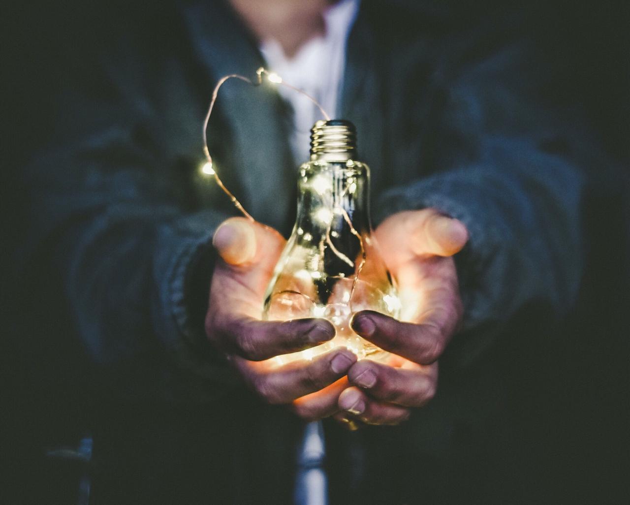 A man holds a lightbulb full of fairylights in cupped hands